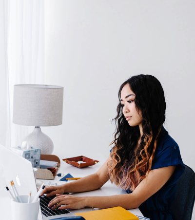 Woman with long black hair dyed at the ends looking pensive as she types on her laptop